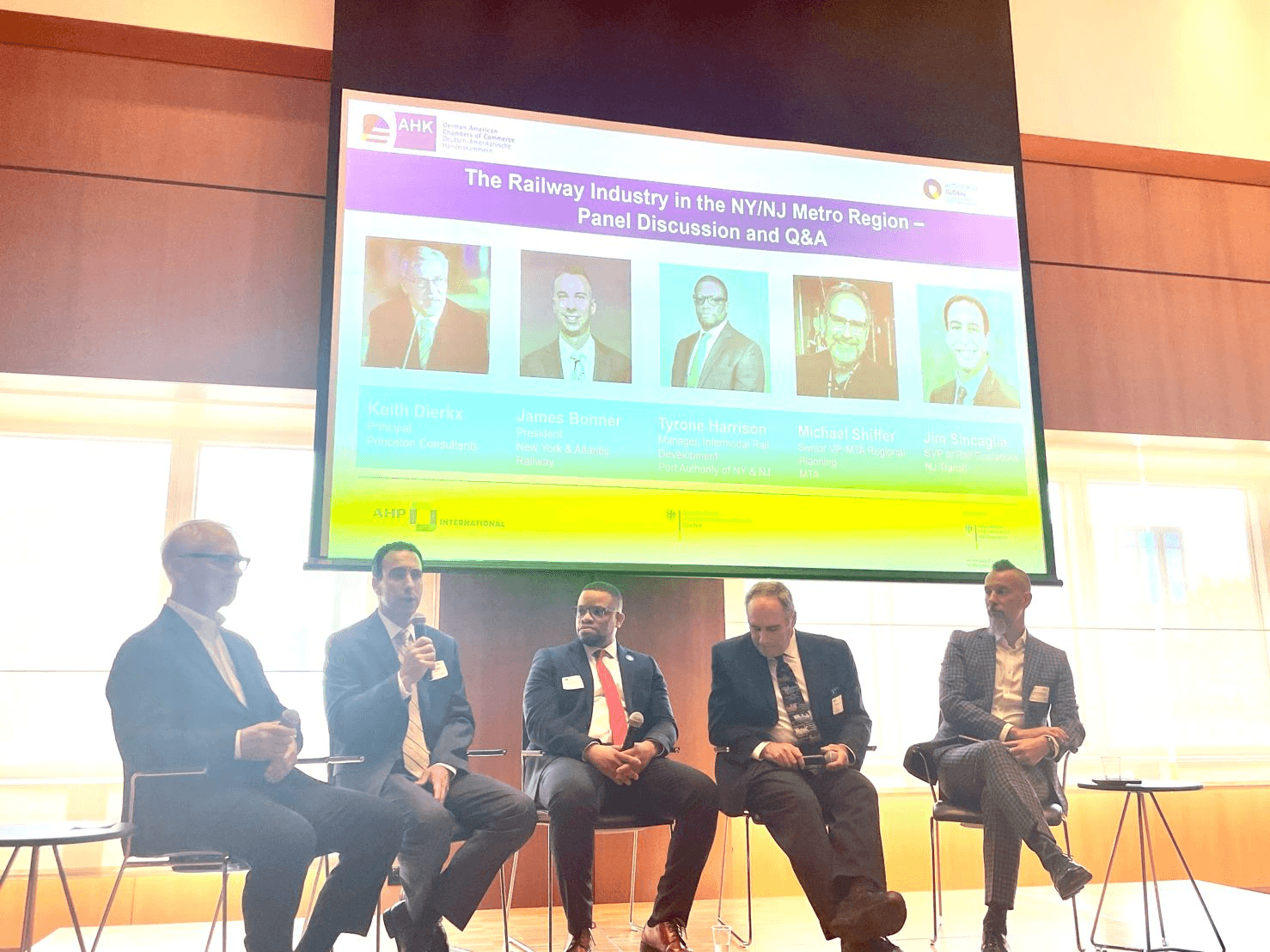 Tyrone Harrison seated third from left on a five-person railway panel, with the session title projected behind the stage